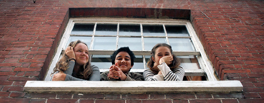 Three Brockwood Park School students looking from a window smiling